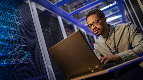 IT support technician using a laptop computer for server maintenance in a data center.